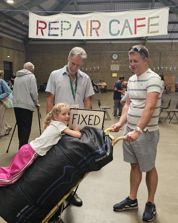 A young visitor with a FIXED sign under the Repair Cafe banner